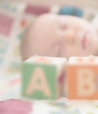 A sleeping baby's face with wooden play blocks in front of his face with an A and a B on each block. The picture is very soft and slightly transparent.